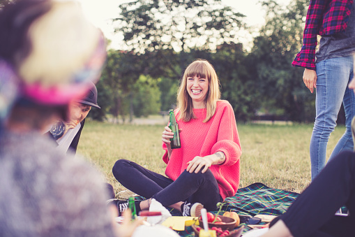 Shot of cheerful young woman enjoying a day outdoors with friends, picnic at park.
