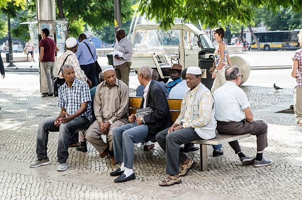 Tangier, Morocco - February 2, 2014: Two men have a rest on a sidewalk outside a mosque, one seats on a vase, the other leans on a small tree. On the wall a holy script from Coran.