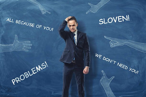 istock Embarrassed businessman standing near dark blue wall with hands pointing 625392092