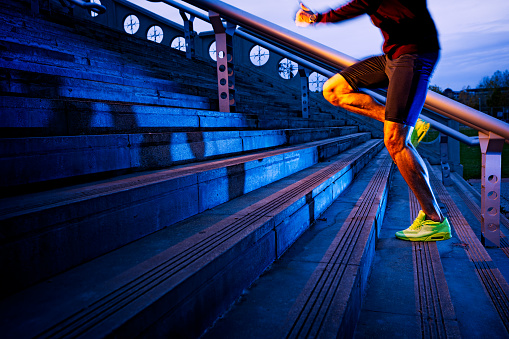 Athletic legs of young sport man with sharp scarf muscles running on staircase steps, jogging in urban training workout. Runner competition in fitness and healthy lifestyle concept