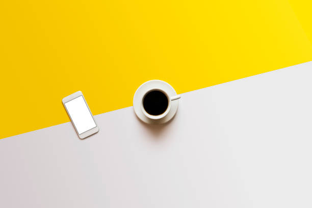 Coffee in white cup and blank screen white phone on white yellow color block background. Top view shot.