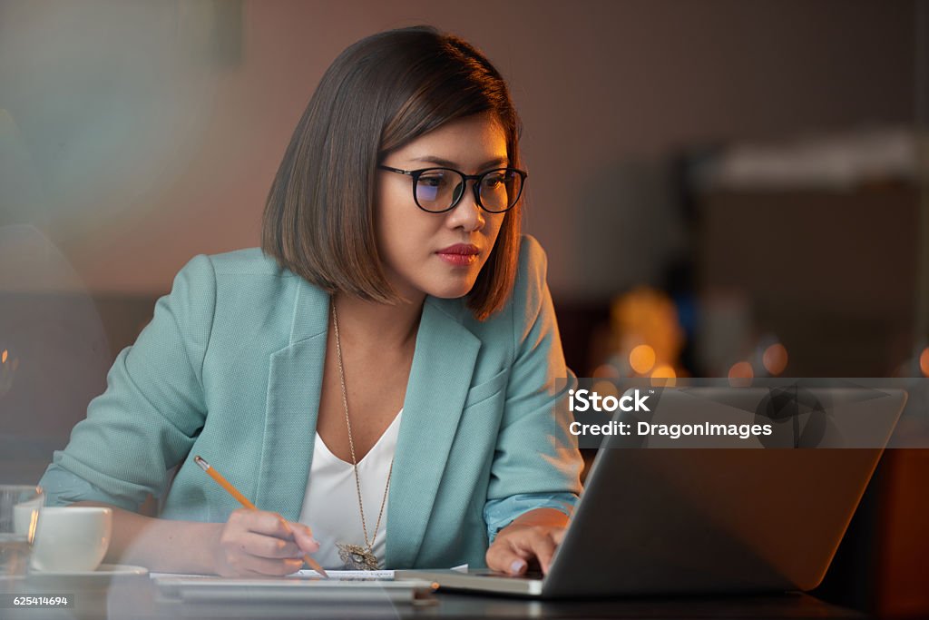 Busy lady Young Vietnamese business woman working on laptop and taking notes Laptop Stock Photo