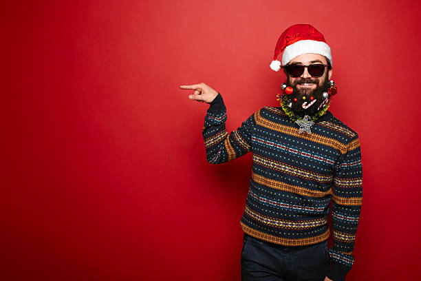 istock Bearded hipster man in santa hat gesturing to left 625415696