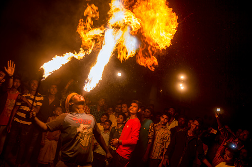 Delhi, India - April 13, 2016: Artists perform and show their skills at the Gajan Festival. In this image a young man breathes a large ball of fire by spitting kerosene from his mouth.