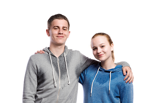 Teenage boy and girl in sweatshirts, with arms around each other. Studio shot on white background, isolated.
