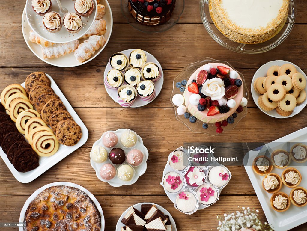 Table with cakes, cookies, cupcakes, tarts and cakepops. Table with cake, pies, cupcakes, tarts and cakepops. Studio shot on brown wooden background. Flat lay. Cake Stock Photo