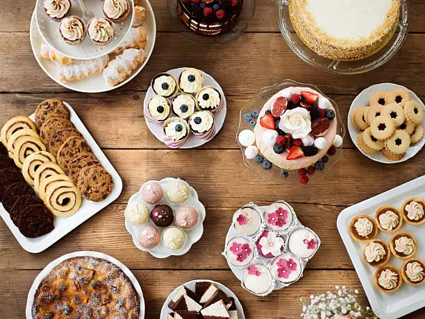 Table with cake, pies, cupcakes, tarts and cakepops. Studio shot on brown wooden background. Flat lay.
