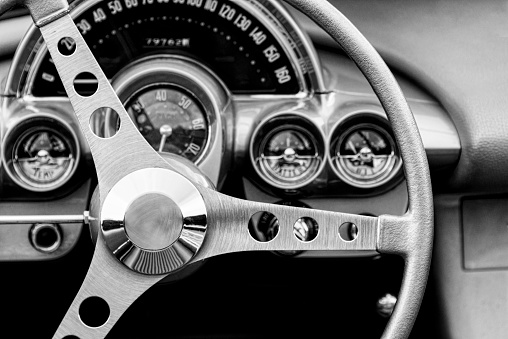 Monochrome image of the steering wheel and interior of a classic car.