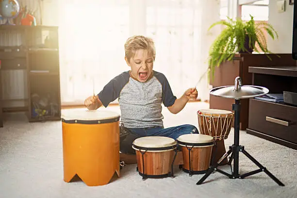 Little boy aged 7 playing little drums in his room. The drums are very noisy and the boy also screams.