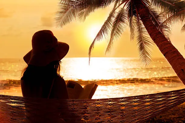 Woman reading  in hammock at stunning sunset during vacation in phuket