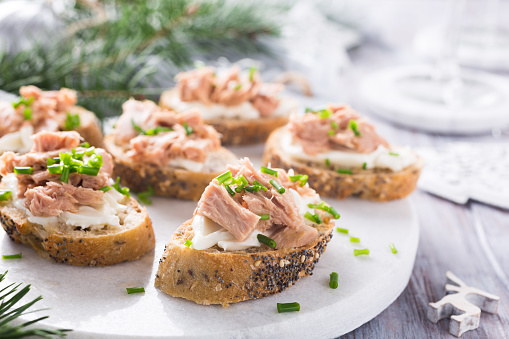 Slices of baguette with fresh tuna, cream cheese and chopped onion chives on marble board. Christmas themed dinner table.