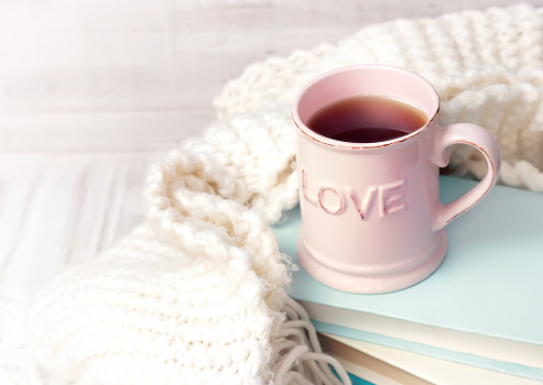 Pink coffee tea mug on stack of books with knits vintage background empty space for text. Valentine's day holiday icon. Retro  literature concept.