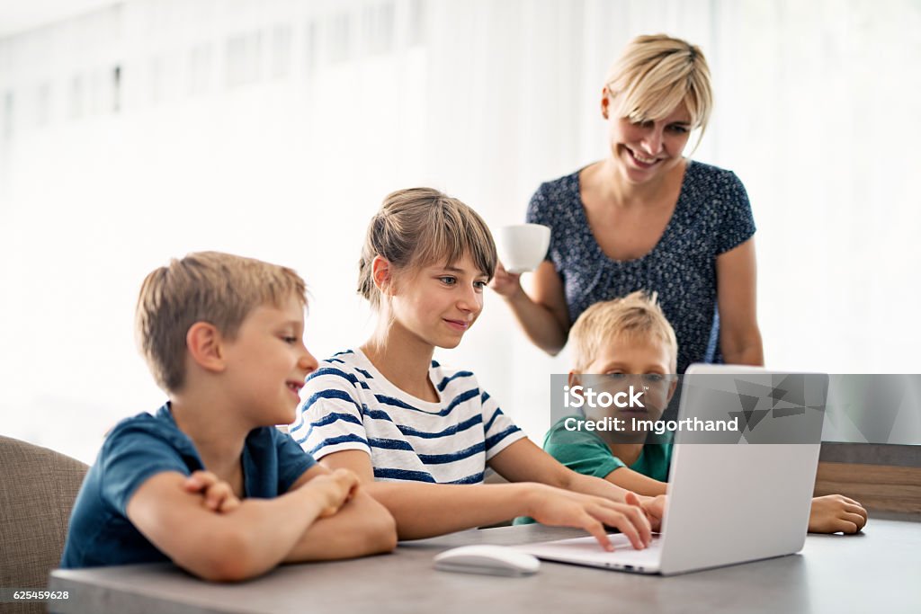 Family using modern ultrabook computer Family using modern ultrabook computer. Mother with 3 kids are using laptop computer and having fun. Family with Three Children Stock Photo