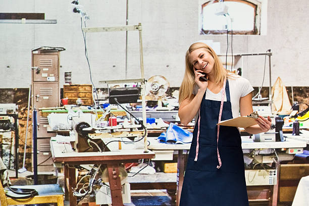 istock Smiling seamstress on phone in textile industry 625490180