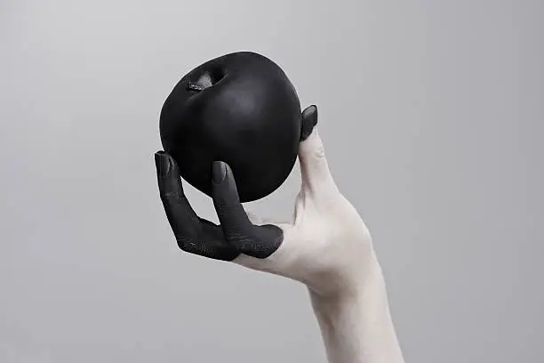 Studio shot of a woman's hand holding a black apple