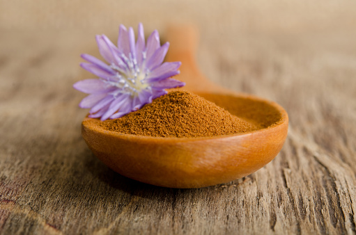 Blue chicory flower and full wooden spoon of powder  instant chicory on old wooden table
