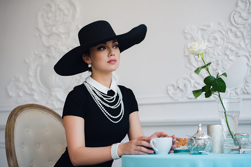 Woman in hat, much like the famous actress, croissant eating and drinking tea