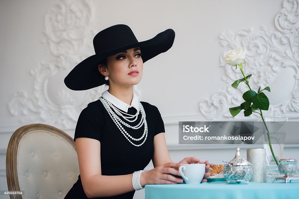 Woman in hat, much like the famous actress, croissant eating Woman in hat, much like the famous actress, croissant eating and drinking tea Women Stock Photo