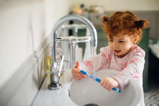 Little girl in the bathroom of her home in her pyjamas. She is rinsing off her toothbrush after brushing her teeth.