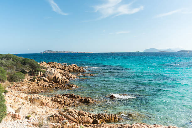 Rocks on the beach natural framing turquoise seascape woth a small speed boat in the center of the image and many other small islands in backgound, on La Maddalena, Italy.