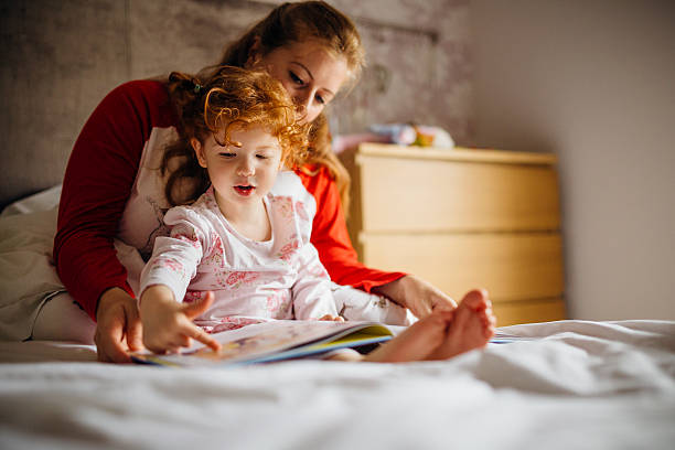 Storytime with Mum Little girl reading a bedtime story with her Mother in her bed. They are sitting together and the little girl is pointing at one of the pictures. double bed photos stock pictures, royalty-free photos & images