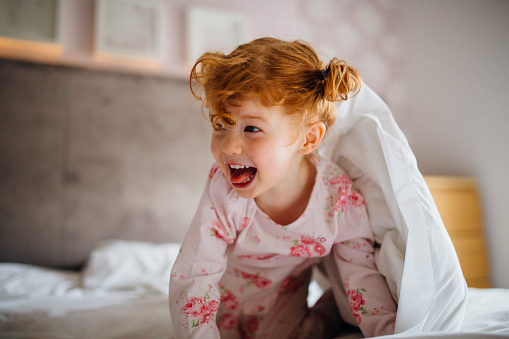 Little girl appearing from under a bed sheet. she is on all fours and is imitating a 'roar' at someone outside of the frame.