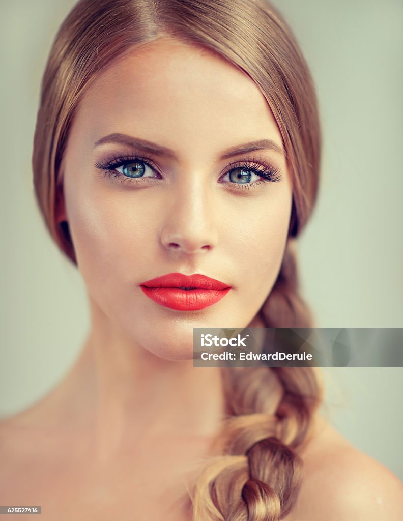 Portrait of beautiful young woman with braid(pigtail) and blue eyes. Close up portrait of beautiful young woman with braid(pigtail), bright red lips and blue eyes. Fashion ,beauty and cosmetic. Make-Up Stock Photo