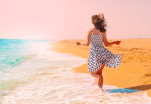 Young happy woman running on the beach back to camera. Trendy rose quartz colored