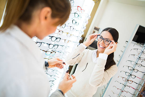 광학 상점에서 안경을 쓰려고 하는 여성 - 광학 기기 뉴스 사진 이미지