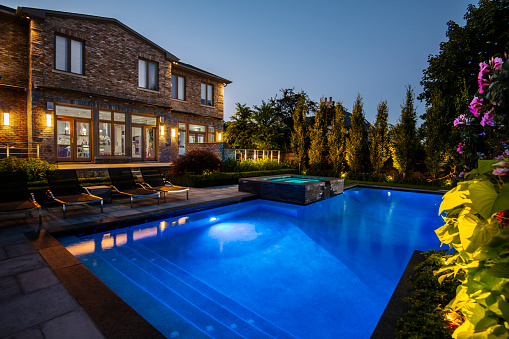 Toronto, Ontario, Canada- July 18, 2016. Luxury North American residence. Back yard with large swimming pool and rear deck. Reflection on the pool at night at Luxury Villa in Toronto, Canada. This space is completely renovated with new interior design and rear yard layout with pool, art work and furniture. High end property is located in North End  of the city,  one of the most desirable and luxury areas minutes away from Yonge Street and  lots of restaurants, shops and places of entertainment.Modern and elegant.