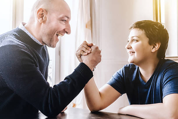 istock french father doing arm wrestling with son at home 625625010