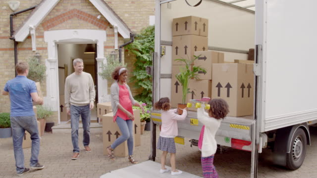 Multi-ethnic family unloading boxes and belongings from moving truck moving into new house