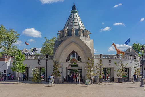 Budapest, Hungary - April 20, 2016: People walking through the entrance gates of Budapest Zoo in Budapest. The sun is shining on a warm spring day.