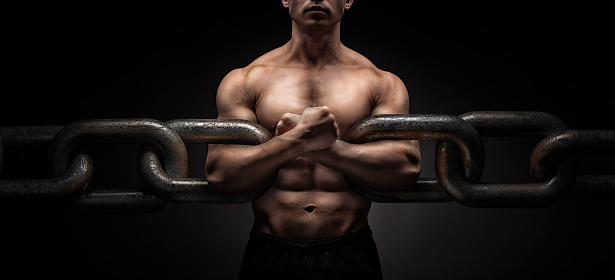 Broken Chain - Freedom Concept . Brutal man bodybuilder athlete holding a chain on a black background. metaphor 