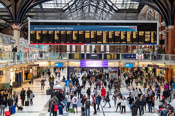 Main entrance hall of Liverpool Street train station in London, UK. People are rushing by, train destinations are shown on the arrival/departure board. Liverpool Street station serves as a major train and subway hub in the East of the City of London, horizontal orientation, England, UK.