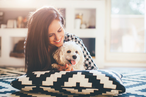 Hipster woman playing with her puppy while lying on the floor