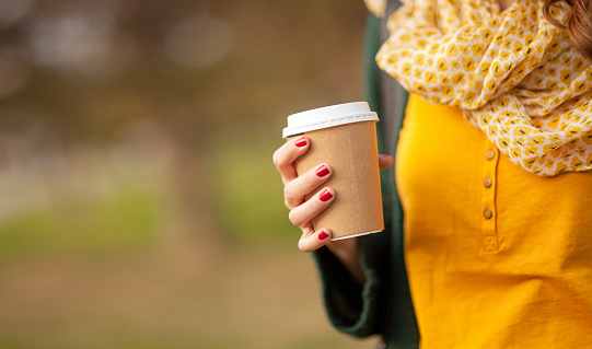 Close up of young woman holding a cup of takeaway coffee cup, shallow depth of field
