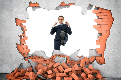 Businessman ruins a brick wall with his leg isolated on the white background. Decisive actions. Brandnew business ideas. Destruction of impediments.