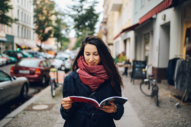 Vintage toned portrait of a young woman in Berlin, wearing a blue coat and a scarf, walking in the Kreuzberg district in the late Autumn day, reading a street magazine. Street style, casual fashion concept.