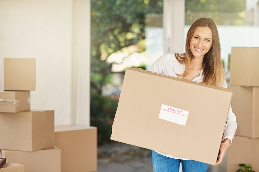 Portrait of a smiling young woman carrying a box on moving into her new house