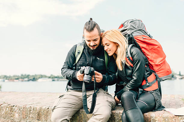 istock Young Couple Backpackers Sitting On Brick Wall And Looking Photos. 625684482