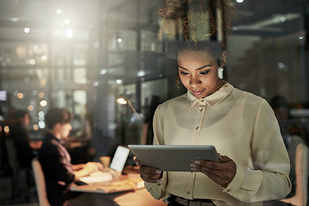 She's taking the lead on this project Shot of an attractive young designer working late at the office with her colleagues in the background working late photos stock pictures, royalty-free photos & images