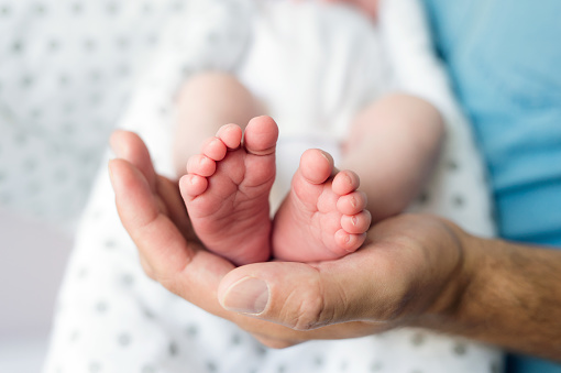 Closeup of cute little baby feet being held by a young mothers hands as she is sitting cross-legged.