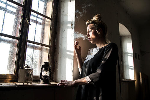 Pensive woman smoking by the window