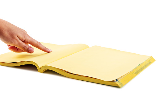 Photo of a hand searching the yellow pages with index finger.