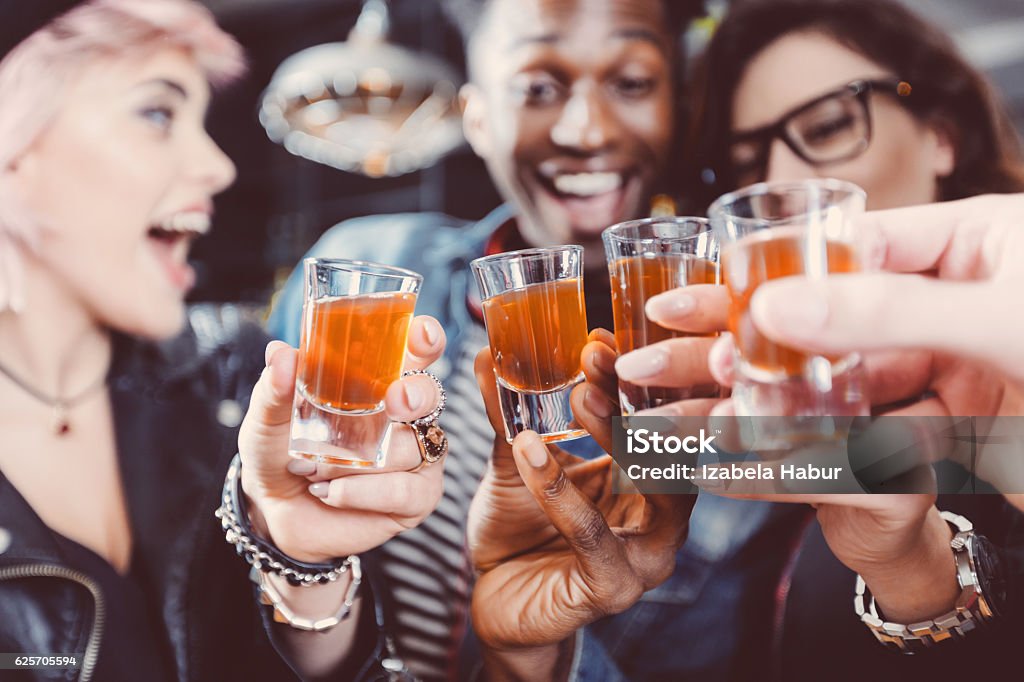 Happy friends drinking shots Multi ethnic group of happy friends - caucasian and afro american - drinking shots in the pub. Focus on hands and shot glasses. Shot Glass Stock Photo