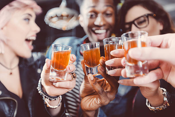 Happy friends drinking shots Multi ethnic group of happy friends - caucasian and afro american - drinking shots in the pub. Focus on hands and shot glasses. tequila drink stock pictures, royalty-free photos & images