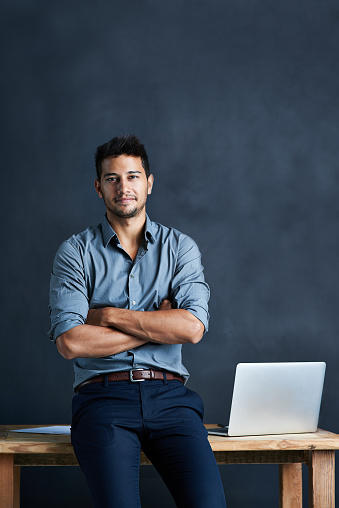 Portrait of a handsome young businessman standing in front of a desk against a dark background