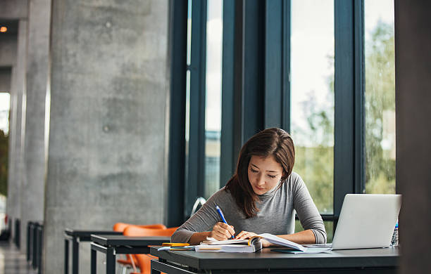 Asian student studying in library Shot of young asian female student sitting at table and writing on notebook. Young female student studying in library. jacob ammentorp lund stock pictures, royalty-free photos & images