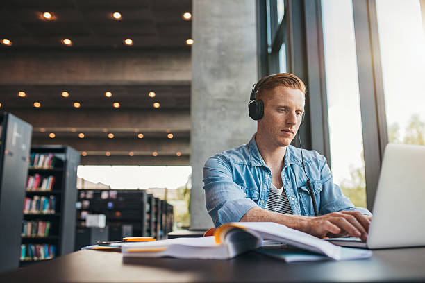 istock Male student working on laptop at public library 625733420